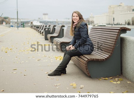 The girl is sitting on the bench. Perspective from the benches. Brunette. Autumn. Wearing Spring