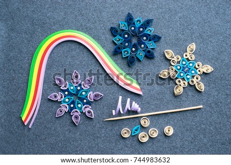 Paper quilling Christmas Crafts in the form of snowflakes from strips of paper. Tools and materials for Christmas quilling diy on a gray felt background. The process of creating Christmas decorations