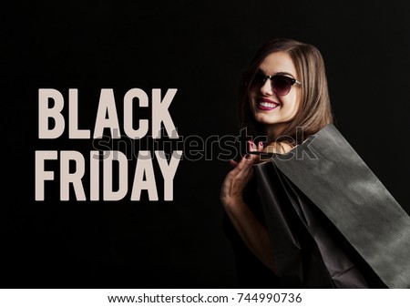 Elegant brunette woman wears sunglasses and black dress holding black shopping bags, black friday concept