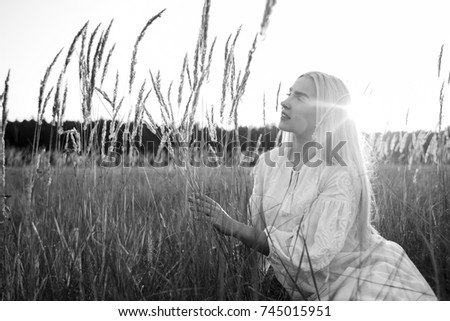 Beautiful girl in a white dress at sunset in a field. Beautiful girl is walking in nature. Portrait at sunset, yellow light, beautiful background, black and white photo