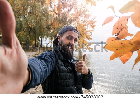 bearded man smiling looking at camera take photo with wide angle camera, self portrait picture thumb up
