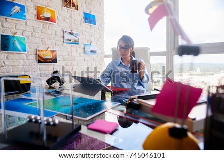 Young person, small business, technology. Busy woman working as photographer in studio, holding coffee mug. Girl with computer laptop for photo editing. Artist doing art production