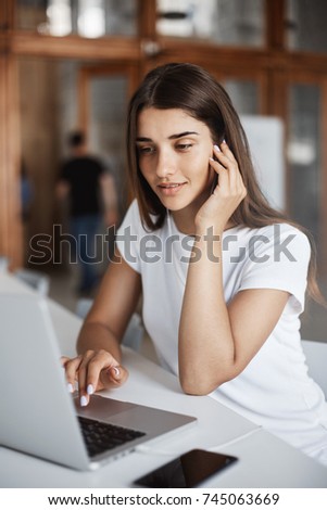 Portrait of beautiful lady using a laptop computer to search internet for new articles and knowledge sitting in bright coworking space.