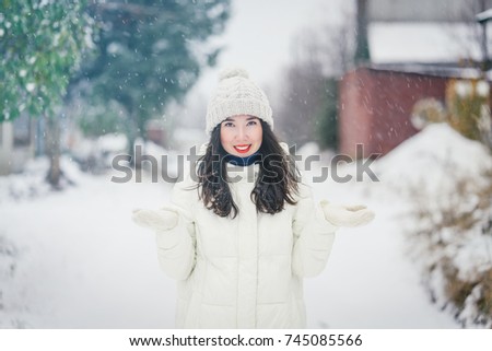 Young beautiful happy smiling girl outdoor catching snowflakes. Snowfall. Christmas, New Year, winter holidays concept.Toned picture.