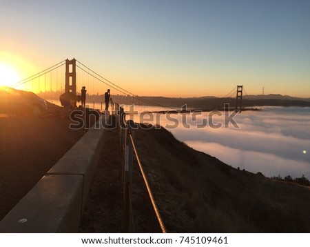 Early morning view of a beautiful sunrise from Mount Tamalpais of low fog coming in under the Golden Gate Bridge in San Francisco with people and photographers looking at the spectacular view