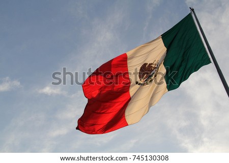 A large Mexican flag (Spanish: Bandera de México), reverse side, lit with golden pre-sunset light, on a flag pole, with a blue sky, in the Zocalo, Mexico City Royalty-Free Stock Photo #745130308