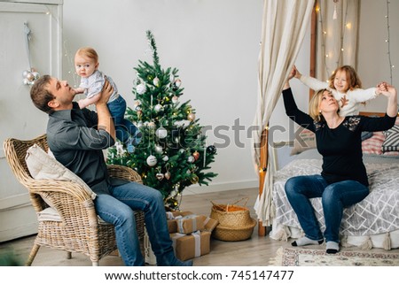 Young happy family of four near christmas tree. Mother with daughter on bed and father with son on armchair. Happy new year concept.