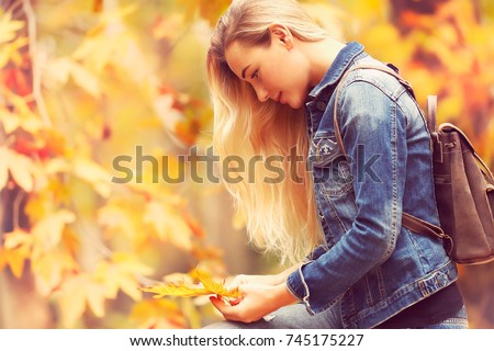 Beautiful model in autumn park, attractive female standing side view and posing over autumnal background, enjoying fall nature

