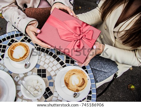 Happy birthday! Top view of beautiful woman giving present to best friend while sitting in french vintage cafe. Receiving gift from friend. Birthday celebration in restaurant. Women holding gift box