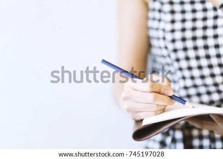 Young woman writer wearing black and white dress, is writing important content idea on notebook, note, laptop with pencil. Remind schedule memory before meeting with coworker. Content concept   Royalty-Free Stock Photo #745197028