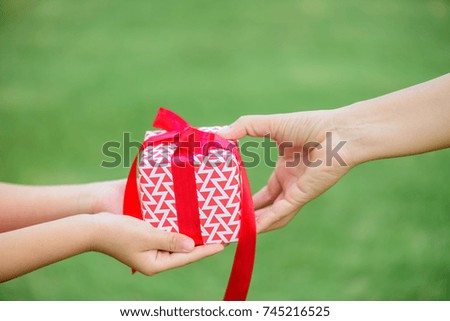 Mother hand giving a gift box with red ribbon to her child. Holidays, present, christmas, and happiness concept.