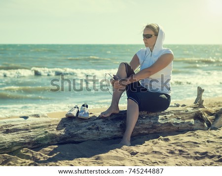 Woman in sportswear on a log at the beach. Morning sun after a workout.