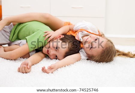 Happy kids boy and girl wrestling in their room laying on the floor - focus on the girl