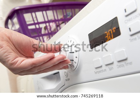 Hand adjusting the temperature setting of a clothes dryer by turning a knob Royalty-Free Stock Photo #745269118