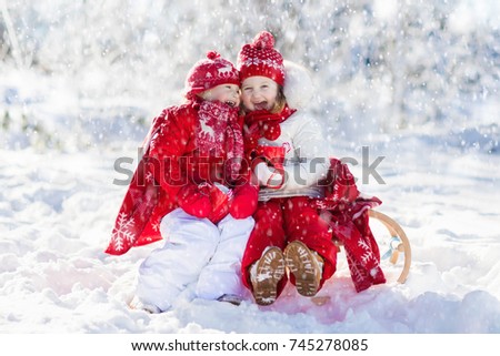 Kids sledding in winter forest. Children drink hot chocolate on sled under warm blanket. Boy and girl play in snow on Christmas vacation. Xmas family fun. Kid with cocoa on sledge. Child with sleigh.