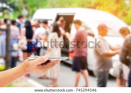 Man use mobile phone, blur image of Chinese tourists are descending from the van as background.