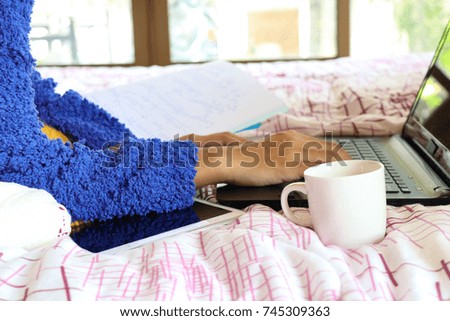 color picture of young women student working report her laptop and drinking coffee on the bed, winter morning