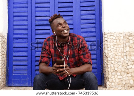 Portrait of happy young african man sitting outdoors with mobile phone and looking away