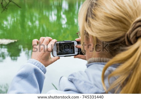 A blonde woman using a phone takes a photo of a beautiful landscape.