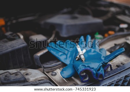 Spark plug. Car candles lie on gloves, in the background the engine