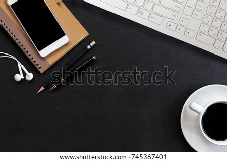 Office desk with white keyboard, smartphone, notepad, pen and hot coffee. Top view of black office desk with copy space. Business desk minimal style concept.
