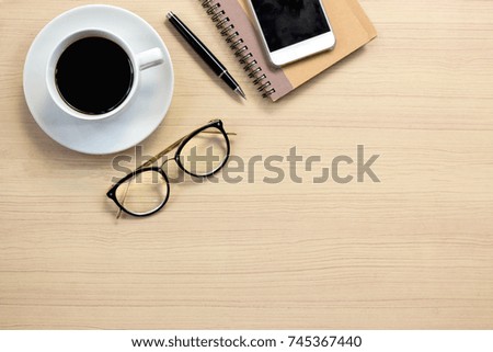 Flat lay of wooden office desk with notepad, smartphone, hot coffee and vintage eyeglasses. Top view with copy space.  Business desk minimal style concept.