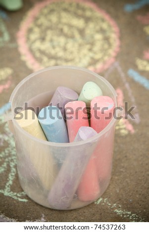 This is a shot of a bucket full of chalk sitting on a sidewalk with a chalk drawing in the background. Shot with a shallow depth of field and vignetting.