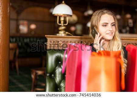 Cute smiling blond woman talking on phone in restaurant after visiting shopping mall