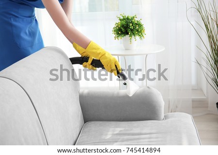 Woman cleaning couch with vacuum cleaner at home Royalty-Free Stock Photo #745414894