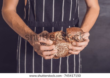 Baker man holding homemade rustic wheat bread in hands. Selective focus.