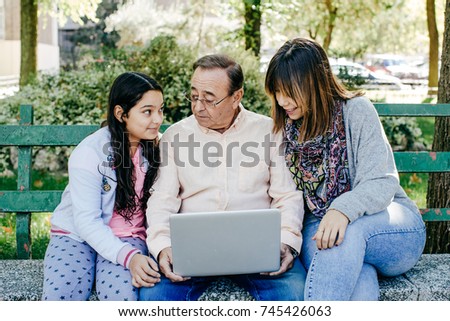 
A father with his daughters sitting on a stone bench, using their mobile phones. Relaxed autumn day in family outdoors whit their pet. Lifestyle portrait.

