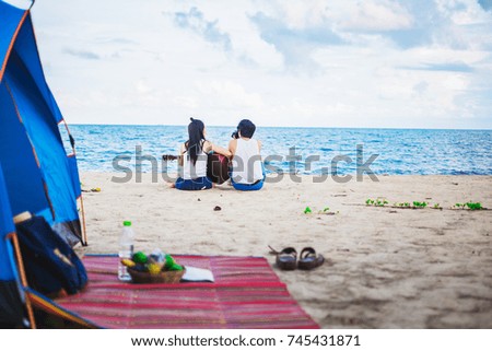couple traveler playing a guitar and taking photo on the beach for vacation foreground is tent and picnic thing for camping.