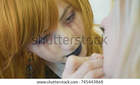 Beautiful girl artist with halloween makeup at work. Process applying halloween makeup on model's face.