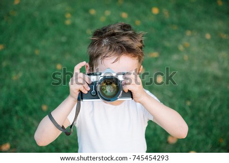funny cute kid wants to take a picture with his vintage film camera on green grass backdrop with some fallen leaves