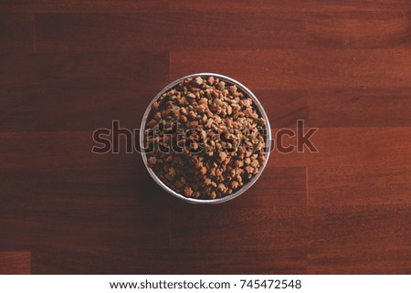 Dry animal food in stainless bowl on on parquet wood floor, top view.