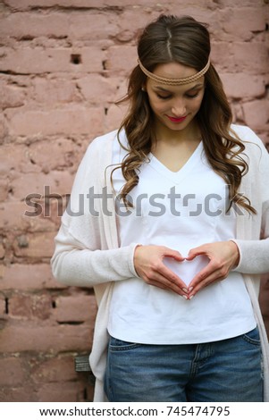 Young beautiful woman pregnancy, heart from the hands, heart, on pink background, love