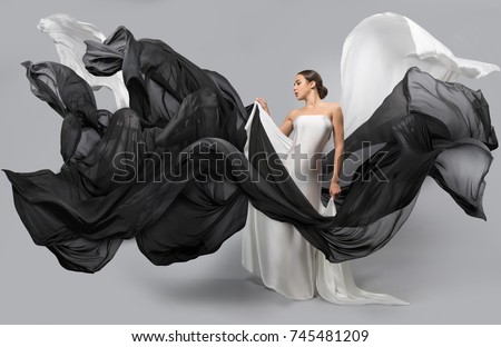 fashion portrait of a beautiful woman in a white and black dress. The fabric flies in the wind. Women silhouettes visible through it.