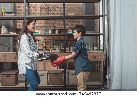 Young woman with punching pads on hands and her little son in boxing gloves making a celebratory gesture