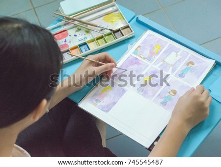 Student teenage girl hands drawing cartoon in watercolor about her teen life on blue table.