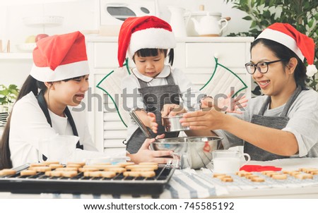 Happy Asian family wear Santa hats preparing the dough bake cookies for Christmas in the kitchen.