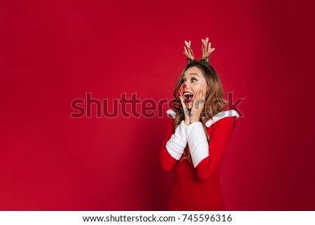 Photo of surprised young woman wearing christmas deer costume standing isolated over burgundy background wall. Looking at copyspace.