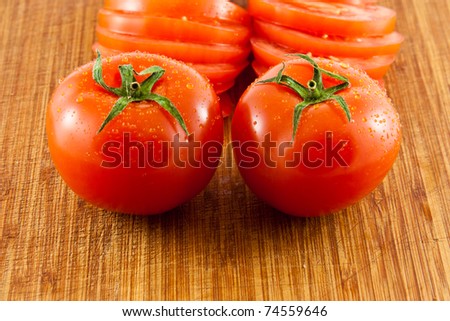 Picture of two tomatoes on a wooden board with sliced tomatoes in the back