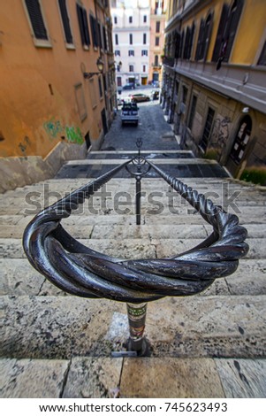 Stone stairs with metal vintage handrails as seen from above close up with blurred background of a narrow street between the buildings in Rome, Italy