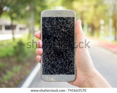 Close-up image of human hand holding old broken and cracked screen smartphone on street background