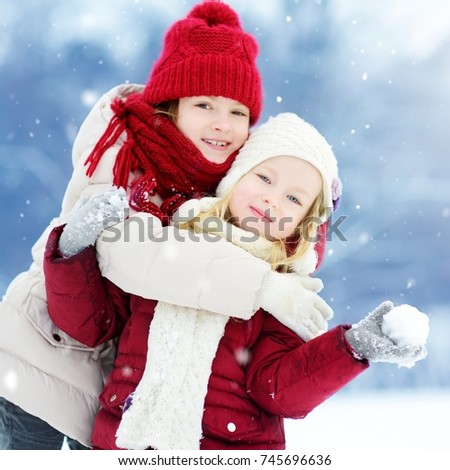Two adorable little girls having fun together in beautiful winter park. Beautiful sisters playing in a snow. Winter activities for kids.