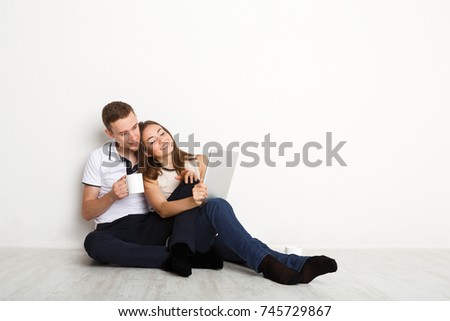 Young couple web surfing on laptop sitting on floor in empty living room of new apartment on white background, copy space