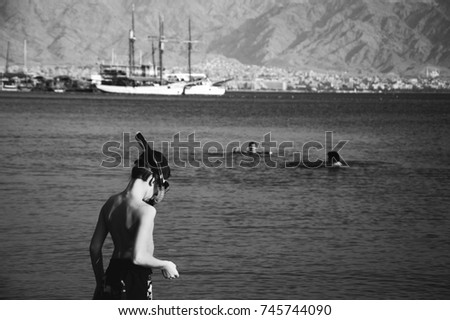 Eilat, Israel. Boy is going to snorkel. Winter sun escape destination. Wooden ship and mountains at background. Black and white photo.