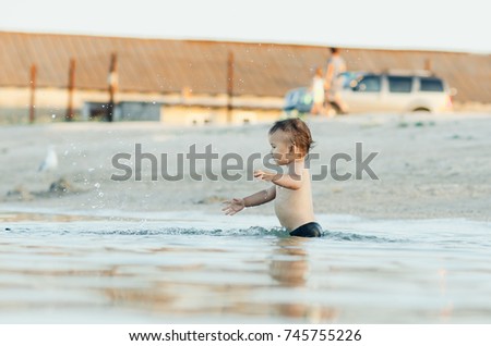 Happy baby playing in the sea, splashing, rejoicing, little