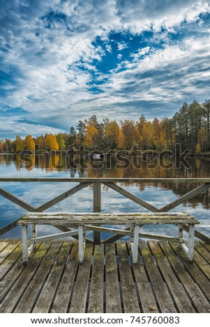 Picture of blue sky over autumn lake and wooden pier with the bench