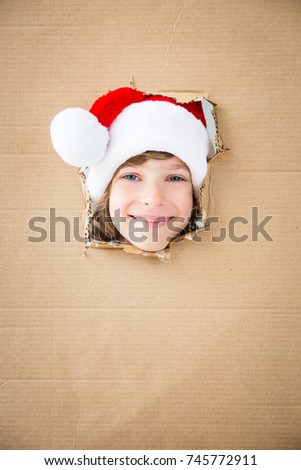 Funny kid looking through hole on cardboard. Child playing at home. Christmas holiday concept. Copy space.